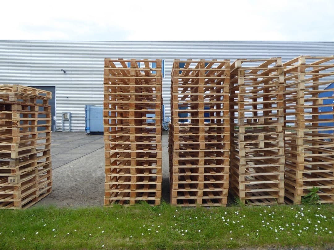 Stacked wooden pallets outside an industrial warehouse, ready for export shipment under a duty drawback claim